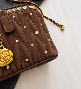 Détail du sac matelassé marron avec breloque camélia doré et bandoulière chaîne