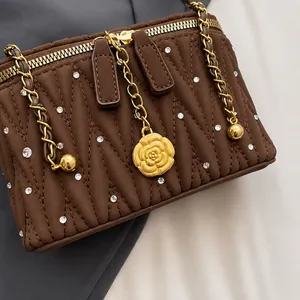 Détail du sac à bandoulière matelassé marron avec cristaux et breloque camélia dorée