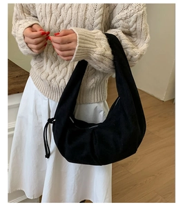 Détail d'un sac hobo noir en daim avec cordon de serrage porté sur un pull en maille