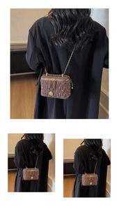 Sac boîte matelassé marron avec chaîne dorée porté sur un tailleur noir