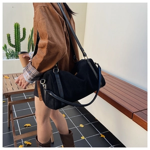 Détail d'un sac Boston en daim noir avec boucles dorées porté par un mannequin en café