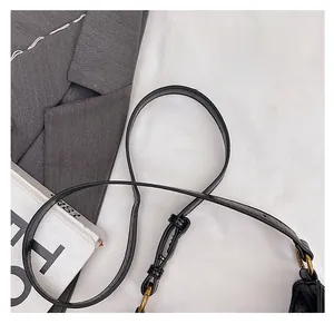 Close-up of black leather bag strap with golden metal buckle on gray blazer