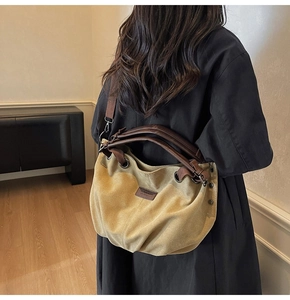 Khaki canvas hobo bag with brown leather strap worn over a black winter coat