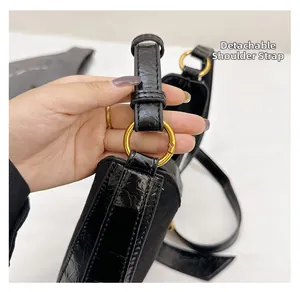 Detail showing the detachable shoulder strap with a golden metal buckle on black embossed leather
