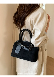 Detail of vintage black suede handbag with metal lock and logo tag on a trench coat