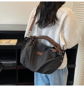 Detail of black canvas tote bag showing brown leather straps and metal rivets on the side