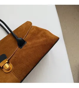 Detail of brown suede tote bag featuring a gold metal lock and contrast black leather handle