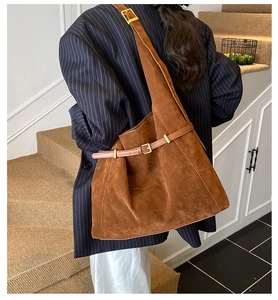 Detail of adjustable leather strap with golden buckle on a brown suede tote bag