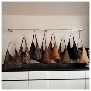 Multiple large suede tote bags in leopard prints and solid colors displayed on a rack