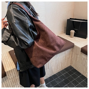 Detail of a large brown suede hobo bag with wide shoulder strap worn by a model