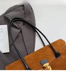 Close-up of brown suede Boston bag with gold buckle detail and thin black shoulder straps