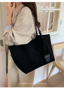 Dettaglio di una grande borsa tote nera opaca con spalline sottili su un trench beige