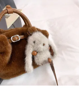 Dettaglio della borsa a secchiello in peluche marrone con trama morbida e ciondolo a coniglio