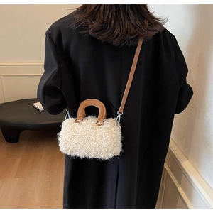 Close-up of white plush crossbody bag with brown leather strap on a black wool coat