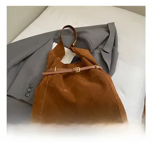 Detail view of brown suede tote bag with decorative leather strap and gold buckle