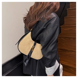 Detailed side view of a beige suede crescent bag with black patent leather strap and trim
