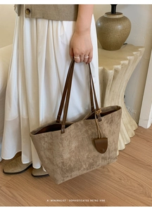 Dettaglio di una borsa tote in pelle opaca marrone con manici eleganti e ciondolo retro