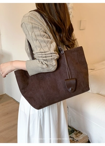 Dettaglio della borsa tote in pelle scamosciata marrone scuro con tracolla in pelle e ornamento