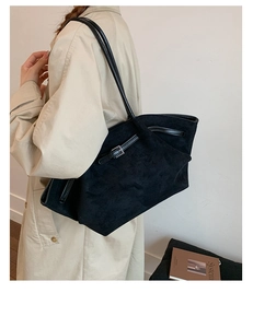 Close-up of black matte leather tote bag with metallic buckle on a beige trench coat