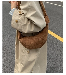 Sac croissant en daim marron porté avec un trench beige sur fond de rue urbaine
