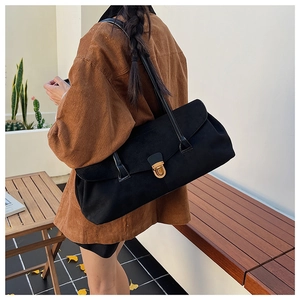 Close-up of a black matte rectangular shoulder bag with gold clasp shown on a model
