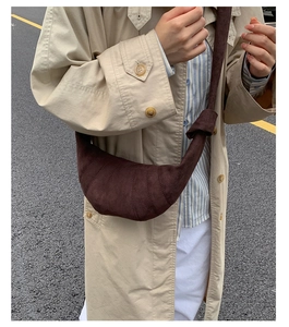 Détail du sac croissant en daim marron foncé montrant les coutures courbées et la texture rétro
