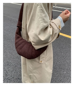 Gros plan d'un sac croissant marron matelassé avec bandoulière nouée sur un trench beige