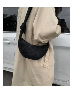 Détail du sac croissant en daim noir avec nœud porté sur un trench-coat beige chic