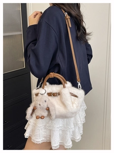 Detailansicht einer weißen Plüsch-Eimertasche mit braunen Ledergriffen und einem Hasen-Anhänger