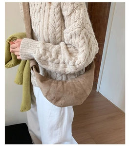 Gros plan d'un sac croissant en daim marron avec surpiqûres sur un pull en maille