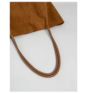 Detail view of brown suede tote bag with durable cylindrical handles and quality stitching