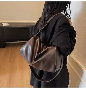Detail of deep brown pleated leather tote bag with glossy texture and wide strap