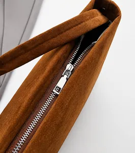 Detailopname van metalen rits en matte textuur op de bruine schouderkussen tas