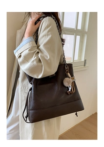 Detail of dark brown quilted tote bag with metal chain strap and soft fur ball charm