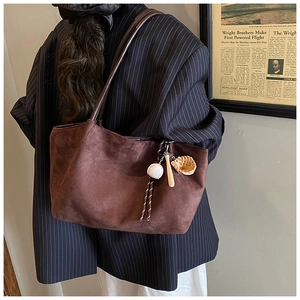 Detalle del bolso tote de ante marrón oscuro con un adorno de béisbol en la correa del hombro