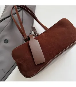 Detail of vintage brown suede pillow bag on grey blazer with a leather logo tag