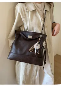 Detail of dark brown leather bucket bag with chain strap and plush monster charm