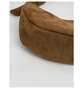 Detailed close-up of reinforced bottom stitching on a brown suede crossbody dumpling bag
