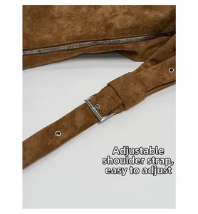 Detail of adjustable suede shoulder strap with silver metal buckle and grommets on brown bag
