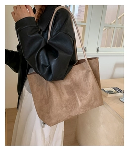 Close-up of a large tan suede tote bag with shoulder straps on a cozy wooden desk