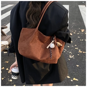 Detalle del bolso tote de ante marrón con colgante de guante y bate de béisbol