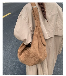 Detail of a brown suede hobo bag featuring silver adjustable buckle on street background