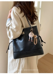 Detail of black leather tote bag with chain strap and quirky plush monster charm