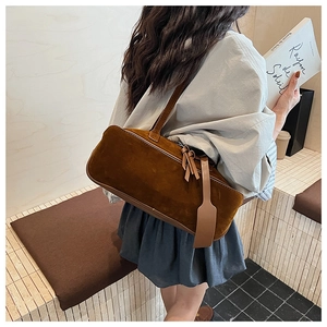Detail of a brown suede cylinder shoulder bag worn by a model in a minimalist setting
