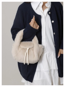 Close-up of fluffy cream plush handbag with leather drawstring detail on a model