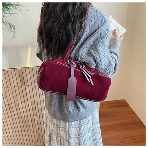 Detail of burgundy suede shoulder bag with metallic zipper and tassel on female model
