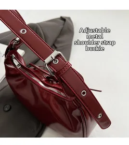 Detail of silver metallic buckle and adjustable strap on a burgundy glossy handbag