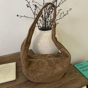 Detail of a large brown suede dumpling bag with a minimalist silver zipper closure