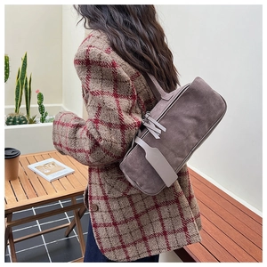 Brown suede tote bag shown on shoulder of a woman wearing a plaid blazer in a cafe