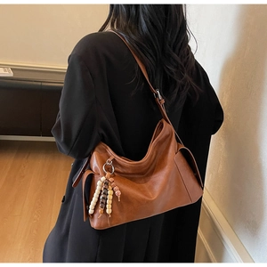 Close-up of brown hobo bag with side flap pockets and a beaded tassel charm detail